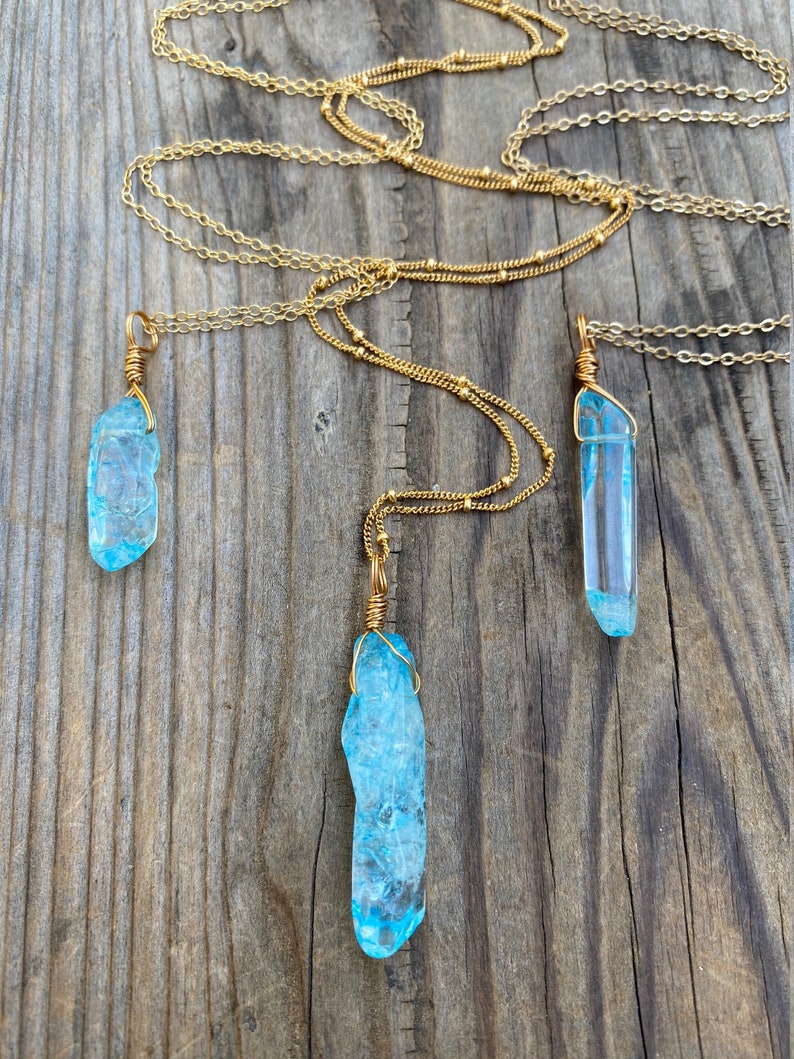Puede incluir: Tres collares de cadena dorada con colgantes de cristal azul. Los cristales est&aacute;n envueltos en alambre dorado y tienen una textura rugosa y natural.