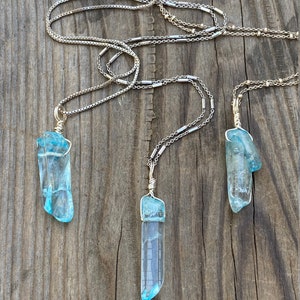 Puede incluir: Tres collares de plata con colgantes de cristal azul. Los cristales son largos y puntiagudos, de color azul claro.