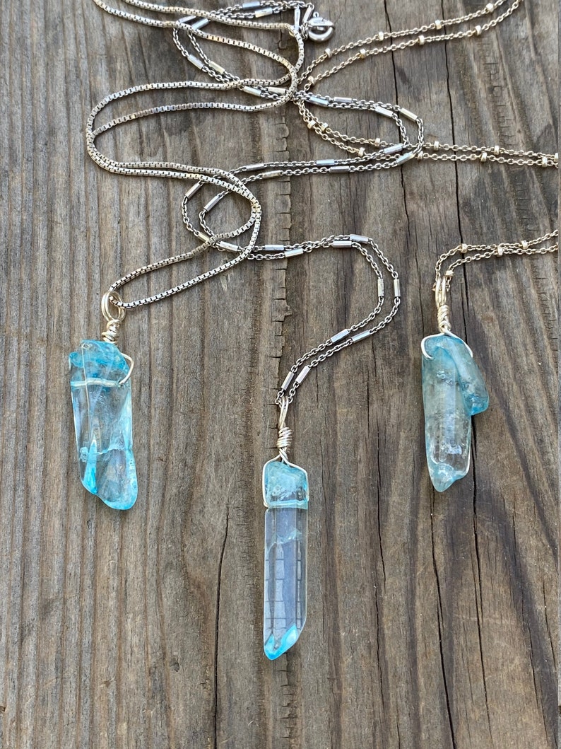 Puede incluir: Tres collares de plata con colgantes de cristal azul. Los cristales son largos y puntiagudos, de color azul claro.