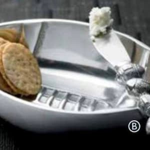May include: A silver football-shaped serving dish with a small knife and a stack of crackers. The knife has a decorative handle.