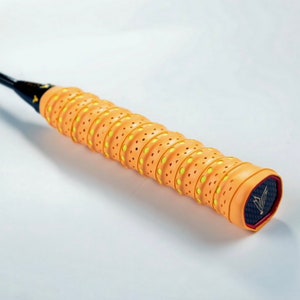 May include: Orange and yellow badminton racket grip with a textured surface and small holes. The grip has a black and red logo with a stylized bird design.