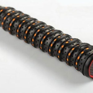 May include: Close-up of a black badminton racket grip with orange and black patterned grip tape. The grip has a textured surface with small holes and a red and black end cap with a logo.