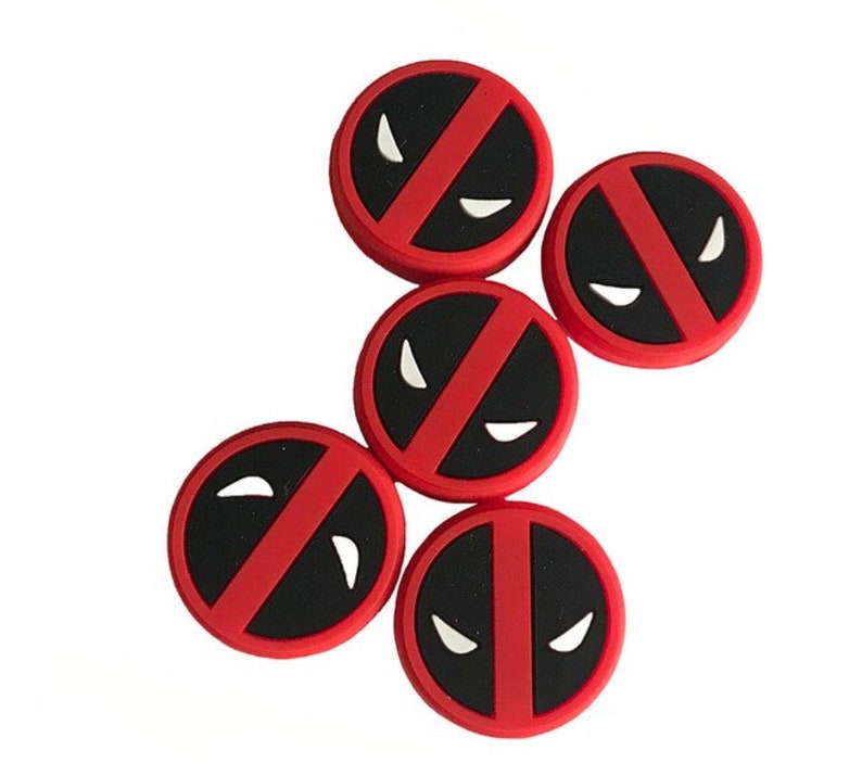 May include: Five red and black round stickers with a white Deadpool logo. The logo features a red slash across a black background with two white eyes.