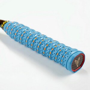 May include: Close-up of a blue and orange badminton racket grip with a black and gold logo. The grip has a textured surface with small holes.