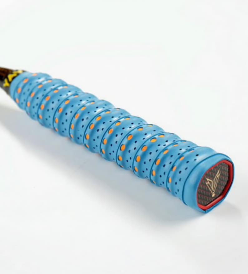 May include: Close-up of a blue and orange badminton racket grip with a black and gold logo. The grip has a textured surface with small holes.