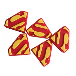 May include: Five red and yellow rubber Superman logos. The logos are shaped like a diamond with a rounded top and bottom.