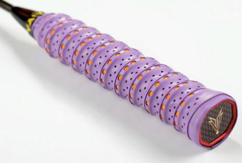 May include: Purple and orange badminton racket grip with a textured surface and small holes. The grip has a black and gold logo with a stylized bird design.