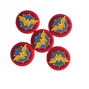 May include: Five red, white, and blue Wonder Woman logo buttons. Each button features a gold Wonder Woman logo with a red star-shaped border and a blue center.