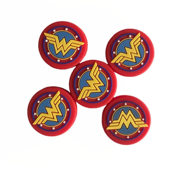 May include: Five red, white, and blue Wonder Woman logo buttons. Each button features a gold Wonder Woman logo with a red star-shaped border and a blue center.