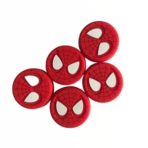 May include: Five red and white silicone thumbstick covers with a Spiderman design. Each cover features a white spider eye design.