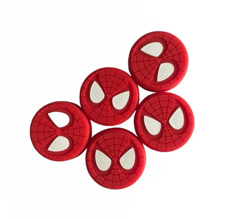 May include: Five red and white silicone thumbstick covers with a Spiderman design. Each cover features a white spider eye design.