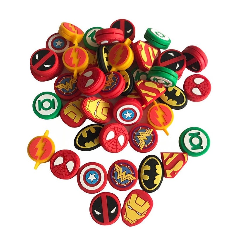 May include: A collection of colorful, round, rubberized gaming console controller caps featuring various superhero logos, including Superman, Batman, Wonder Woman, Iron Man, The Flash, Deadpool, and Green Lantern.