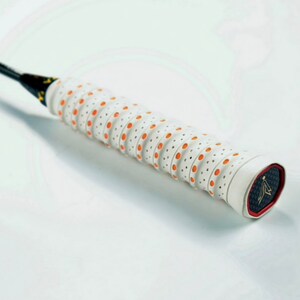 May include: White badminton racket grip with orange dots and a black and gold logo on the end.