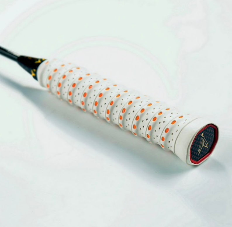 May include: White badminton racket grip with orange dots and a black and gold logo on the end.