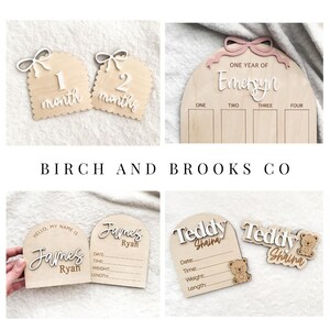 K&ouml;nnte beinhalten: Eine Sammlung von Meilensteinmarkern und Namensschildern f&uuml;r Babys aus Holz. Die Marker zeigen die Zahlen 1 und 2 mit dem Wort "Monate". Die Namensschilder bieten Platz f&uuml;r Babys Daten. Der Text "BIRCH AND BROOKS CO" ist ebenfalls sichtbar.