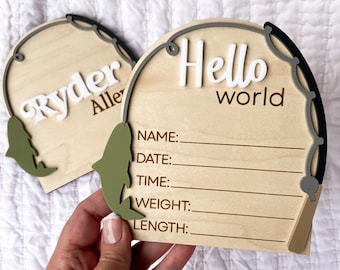 May include: Two wooden baby announcement plaques. One says "Ryder Allen" in white letters. The other says "Hello world" in white letters. Both have a fishing rod design and space to write baby's details.