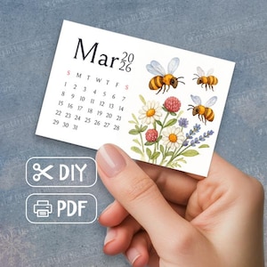 Puede incluir: Una pequeña tarjeta de calendario blanca para marzo de 2026, sostenida por una mano. La tarjeta presenta una ilustración de acuarela de abejas, flores y el texto "Mar 2026". Debajo, las palabras "DIY" y "PDF".