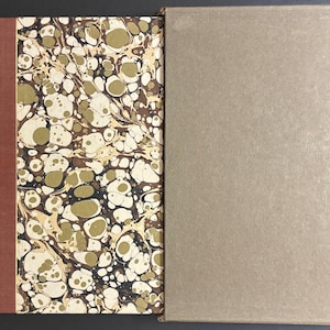 May include: An open book with a marbled cover in shades of brown, cream, and gold. The spine is a solid reddish-brown color. The adjacent cover is a solid tan color.