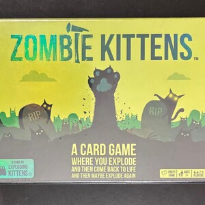 May include: A sealed box for the card game "Zombie Kittens." The box features a green and black illustration of zombie cats rising from graves. The game's title is in large, green, stylized letters. The box also includes the text "A Card Game Where You Explode and Then Come Back to Life and Then Maybe Explode Again."