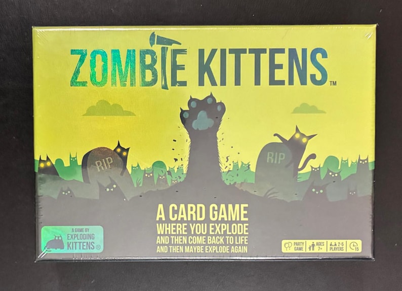 May include: A sealed box for the card game "Zombie Kittens." The box features a green and black illustration of zombie cats rising from graves. The game's title is in large, green, stylized letters. The box also includes the text "A Card Game Where You Explode and Then Come Back to Life and Then Maybe Explode Again."