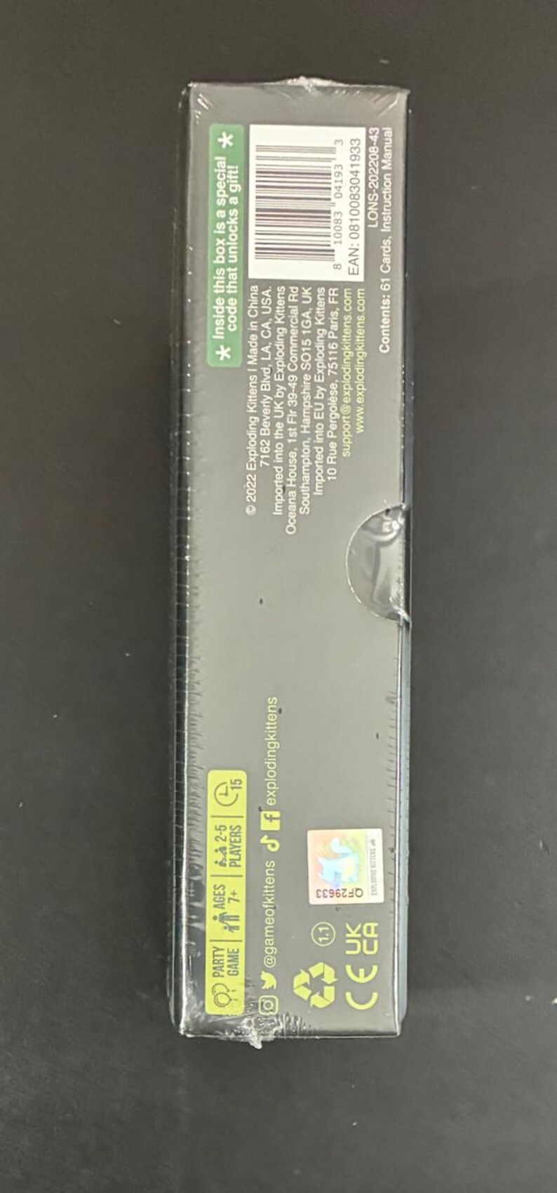 May include: A rectangular box for the Exploding Kittens card game. The box is dark with text that includes the game's name, age range, and player count. It also has a special code for a gift.