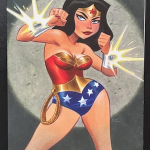 May include: A comic book cover featuring Wonder Woman in a red, gold, and blue costume with a golden lasso. She has black hair, a gold tiara with a red star, and silver bracelets emitting light. The text reads Wonder Woman 80th Anniversary.