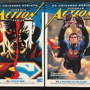 May include: Two DC Universe Rebirth Superman Action Comics graphic novels. The left cover, Vol. 1 Path of Doom, shows a split face of Superman. The right cover, Vol. 2 Welcome to the Planet, depicts Superman flying upward with a city background.