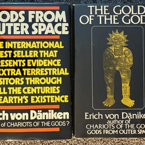 May include: Two hardcover books with black covers. The book on the left is titled "GODS FROM OUTER SPACE" and the book on the right is titled "THE GOLD OF THE GODS". Both books are by Erich von Däniken.