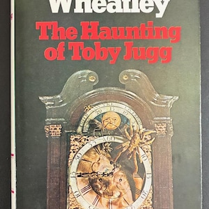 May include: Book cover for "The Haunting of Toby Jugg" by Dennis Wheatley. The title is in red, with the author's name in white. The cover features a detailed illustration of a grandfather clock with a spider and a face on the clock face.