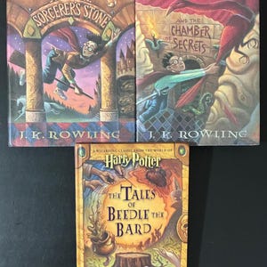 May include: Three hardcover books by J.K. Rowling: Harry Potter and the Sorcerer's Stone, Harry Potter and the Chamber of Secrets, and The Tales of Beedle the Bard. Each book cover features colorful, detailed fantasy illustrations and gold lettering.