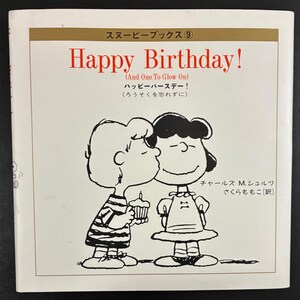 May include: A book cover featuring a cartoon illustration of two characters from the Peanuts comic strip. One character is kissing the other, who is holding a cupcake. The title "Happy Birthday!" is written in red.
