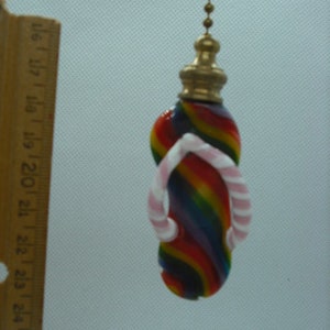 Peut inclure: Un tire-chaîne de lumière en verre coloré en forme de tong avec des lanières roses. Le tire-chaîne est attaché à une chaîne dorée.