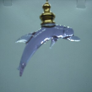 May include: A silver dolphin charm with a gold-colored finial hanging from a white background.