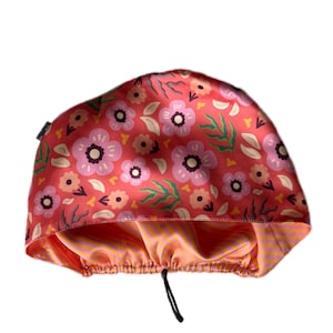 May include: A floral print shower cap with a drawstring closure. The cap features a red background with pink and purple flowers, green leaves, and a yellow and orange striped interior.