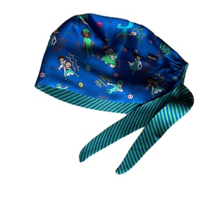 May include: A blue surgical scrub cap with a cartoon superhero design. The cap features a pattern of figures in action poses, with green and blue striped ties. The cap is made of a silky material.