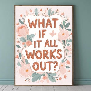 May include: A framed art print with the text "WHAT IF IT ALL WORKS OUT?" in orange letters. The text is surrounded by a floral wreath of pink roses, green leaves, and small blue flowers. The background is a light pink color.