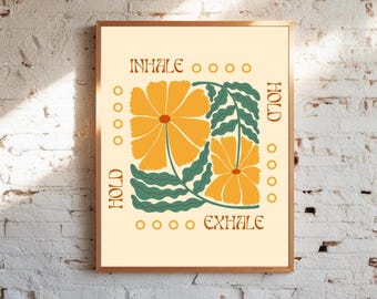 May include: A framed art print featuring a floral design with the words "INHALE, HOLD, EXHALE" in brown text. The artwork showcases two large orange flowers with green leaves against a cream background. The frame is a warm brown color.