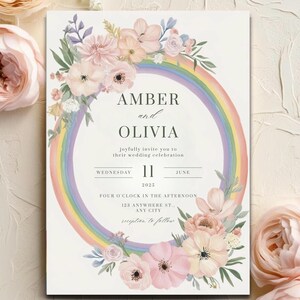 May include: Wedding invitation featuring a rainbow and floral design. The invitation reads "Amber and Olivia joyfully invite you to their wedding celebration. Wednesday, June 11, 2023. Four o'clock in the afternoon. 123 Anywhere St., Any City."
