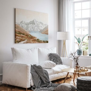 Op de afbeelding: Een witte bank met een zwart-wit gestreept kleed en een kussen. Boven de bank hangt een schilderij van een bergketen met een meer op de voorgrond. Naast de bank staat een gouden staande lamp met een witte kap.