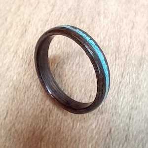 Peut inclure: Une bague en bois noir avec une incrustation turquoise. La bague est lisse et polie.