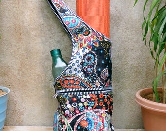 May include: A yoga mat bag with a colorful paisley pattern, holding an orange yoga mat and a green glass bottle. The bag has a zipper closure and a shoulder strap. The text "NEELGARARTS" is visible on the bag.