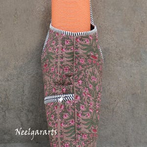 K&ouml;nnte beinhalten: Gesteppte Yogamatten-Tasche mit floralem Muster in Braun, Gr&uuml;n und Rosa. Die Tasche hat eine schwarz-wei&szlig; gestreifte Bord&uuml;re und eine Rei&szlig;verschlusstasche. Eine orangefarbene Yogamatte befindet sich im Inneren. Der Text "Neelgararts" ist sichtbar.