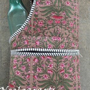 K&ouml;nnte beinhalten: Ein brauner, gesteppter Wasserflaschentr&auml;ger mit einem Blumenmuster in Rosa und Gr&uuml;n. Der Tr&auml;ger hat eine schwarz-wei&szlig; gestreifte Bord&uuml;re und h&auml;lt eine gr&uuml;ne Glasflasche. Der Text "Neelgararts" ist sichtbar.