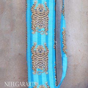 Puede incluir: Una bolsa de yoga azul con un patr&oacute;n a rayas y un estampado de tigre. La bolsa tiene una correa larga para llevarla sobre el hombro.