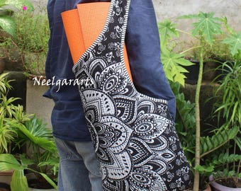 May include: A black and white patterned yoga mat bag with a matching strap is carried over the shoulder. An orange yoga mat is visible inside the bag. The bag has a large, intricate mandala design. The text "Neelgararts" is visible.