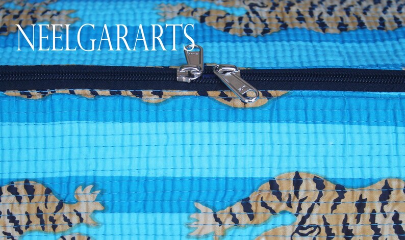 Puede incluir: Primer plano de una cremallera en una bolsa de tela a rayas azules y marrones con estampado de tigre. La cremallera es plateada y tiene un tirador negro. El texto "NEELGARARTS" es visible en la parte superior de la imagen.