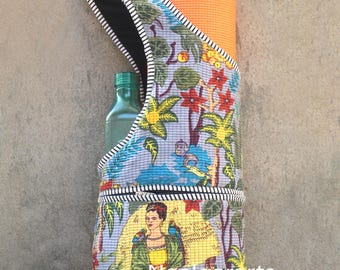 May include: A quilted yoga mat bag with a colorful tropical print, featuring a portrait of a woman. The bag has a black and white striped strap and holds an orange yoga mat and a green water bottle. The bag is designed to carry yoga essentials.