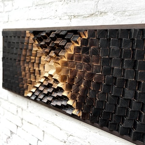 Puede incluir: Una pieza de arte de madera montada en la pared con un diseño geométrico 3D. La pieza está hecha de pequeños bloques de madera cuadrados que están dispuestos en un patrón que crea una sensación de profundidad y movimiento. La madera está teñida de un color marrón oscuro, con algunos de los bloques con un tono más claro, más dorado. La pieza está enmarcada en un marco de madera marrón oscuro.