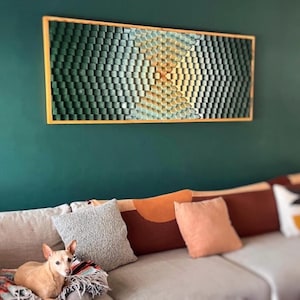 Può includere: Un grande pezzo d'arte da parete rettangolare con un design geometrico. Il design è composto da piccoli pezzi di legno a forma quadrata in tonalità di verde, blu e giallo. Il pezzo è incorniciato in una cornice in legno naturale.