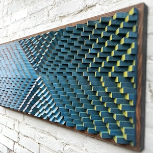 May include: A rectangular wall art piece composed of numerous small, vertical wooden blocks arranged in a geometric pattern. The blocks are stained in shades of deep blue, light blue, and yellow, creating a textured, three-dimensional surface.